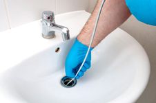 Gloved hand snaking sink drain.