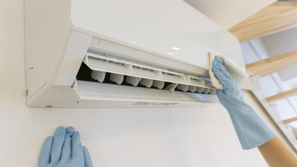 Person cleaning ductless mini-split unit with cloth